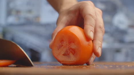 Closeup-of-a-woman-cutting-and-chopping-tomato-by-knife-on-wooden-board